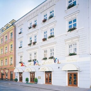 A multi-story hotel with white facades, arched windows, and flower boxes on the balconies. - Hotel Arbes (Prague)