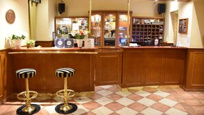 A bar area with wooden counters, two striped stools, a shelf with bottles, and a speaker on the wall. - Hotel Arbes (Prague)