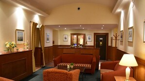 A hotel lobby with a reception desk, seating area with sofas and armchairs, and framed artwork on the walls. - Hotel Arbes (Prague)