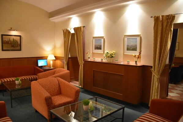 A hotel lobby with a reception desk, two framed pictures on the wall, a sofa, a chair, and a coffee table. - Hotel Arbes (Prague)