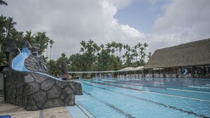 Una piscina con carriles de natación, un tobogán acuático y un edificio con techo de paja.