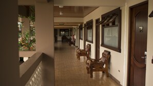 Un pasillo de hotel con bancos de madera, piso de baldosas y una puerta de madera.