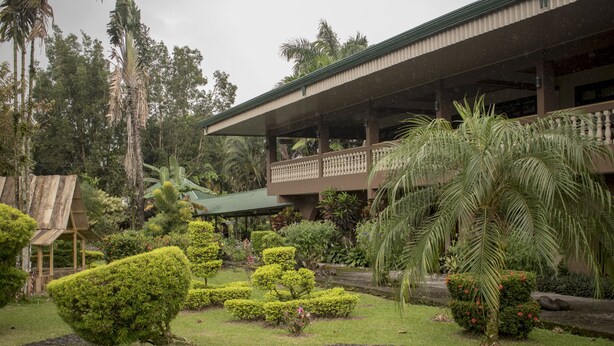 Un edificio con balcón cubierto, rodeado de jardines cuidados y palmeras.