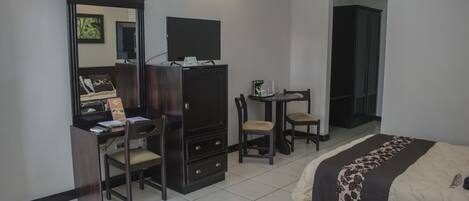 Habitación de hotel con escritorio, silla, televisor, armario y dos camas.