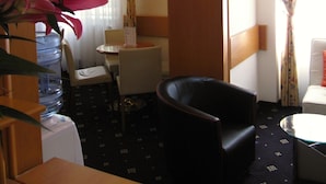 A hotel room with a dining area, a black leather chair, a small table, and a water dispenser. - Hotel Máchova (Prague)
