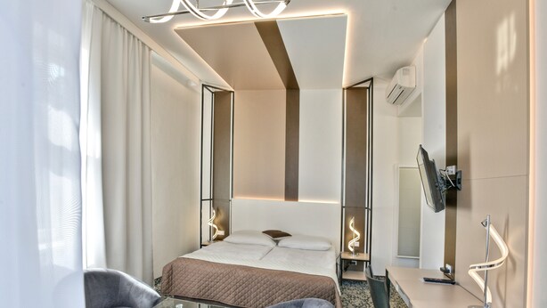A modern hotel room with a bed, two chairs, a desk, and a TV. - Hotel Máchova (Prague)