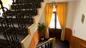 A staircase with ornate black railings, a wooden handrail, and a potted plant on the landing. - Hotel Máchova (Prague)