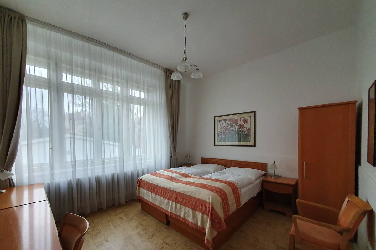 A bedroom with a bed, a desk, a chair, a wardrobe, and a painting on the wall.