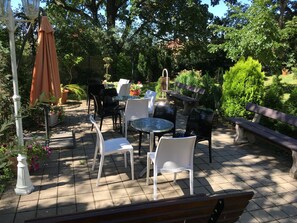 An outdoor patio with tables and chairs, surrounded by greenery and a wooden bench. - Pension Jana - Domov Mládeže (Prague)