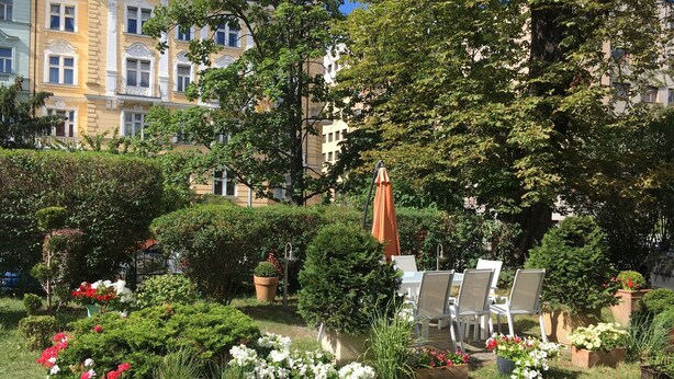 A garden with outdoor seating, surrounded by lush greenery and flowering plants. - Pension Jana - Domov Mládeže (Prague)