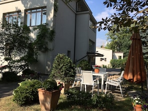 A modern building with a patio area featuring a table and chairs, surrounded by potted plants and a large umbrella. - Pension Jana - Domov Mládeže (Prague)