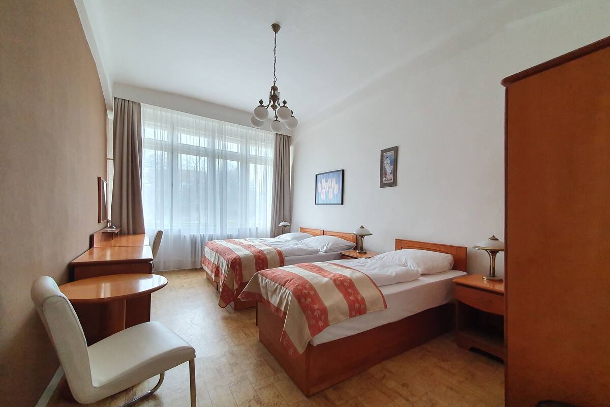 A hotel room with two beds, a desk, a chair, a lamp, and a large window with curtains.