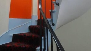 A staircase with black railings and red carpeted steps leading to an orange door. - Hotel Santana (Paris)