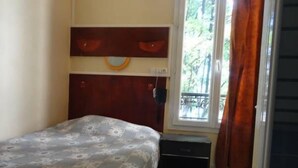 A bedroom with a bed, a small bedside table, a heater, and a window with curtains. - Hotel Santana (Paris)