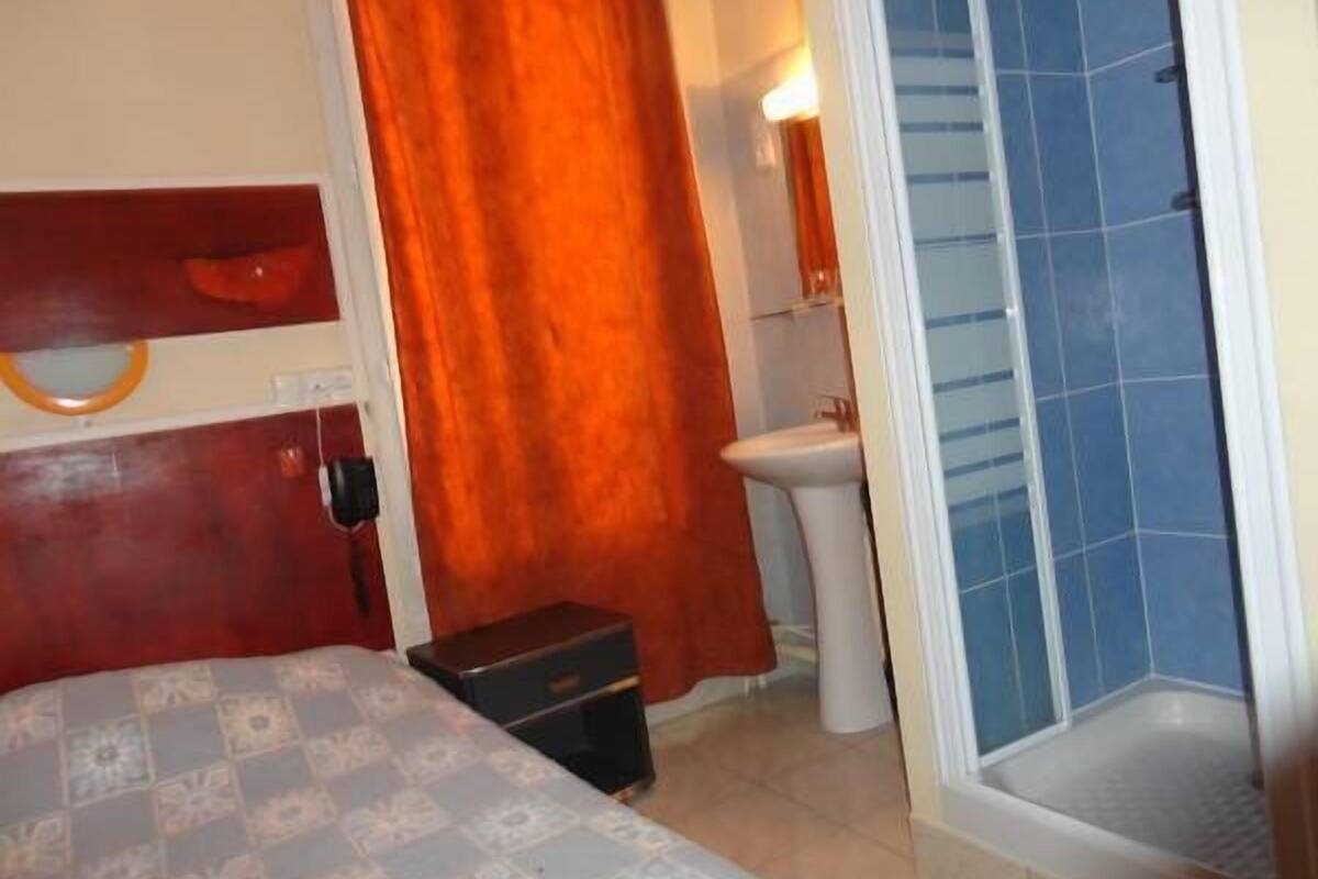 A hotel room with a bed, a small bedside table, a bathroom with a sink and mirror, and a shower area.