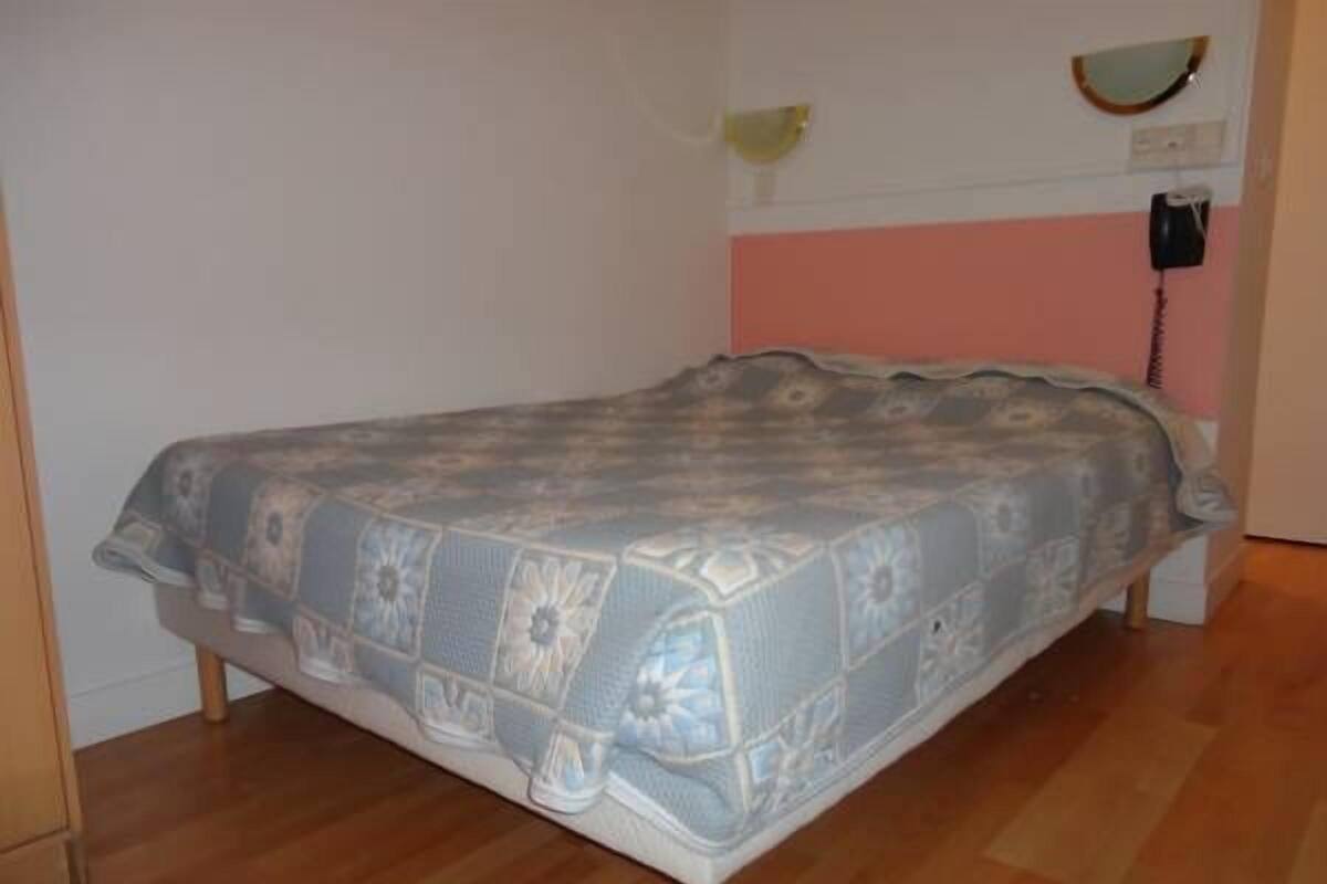 A single bed with a patterned bedspread in a room with wooden flooring and a pink wall.