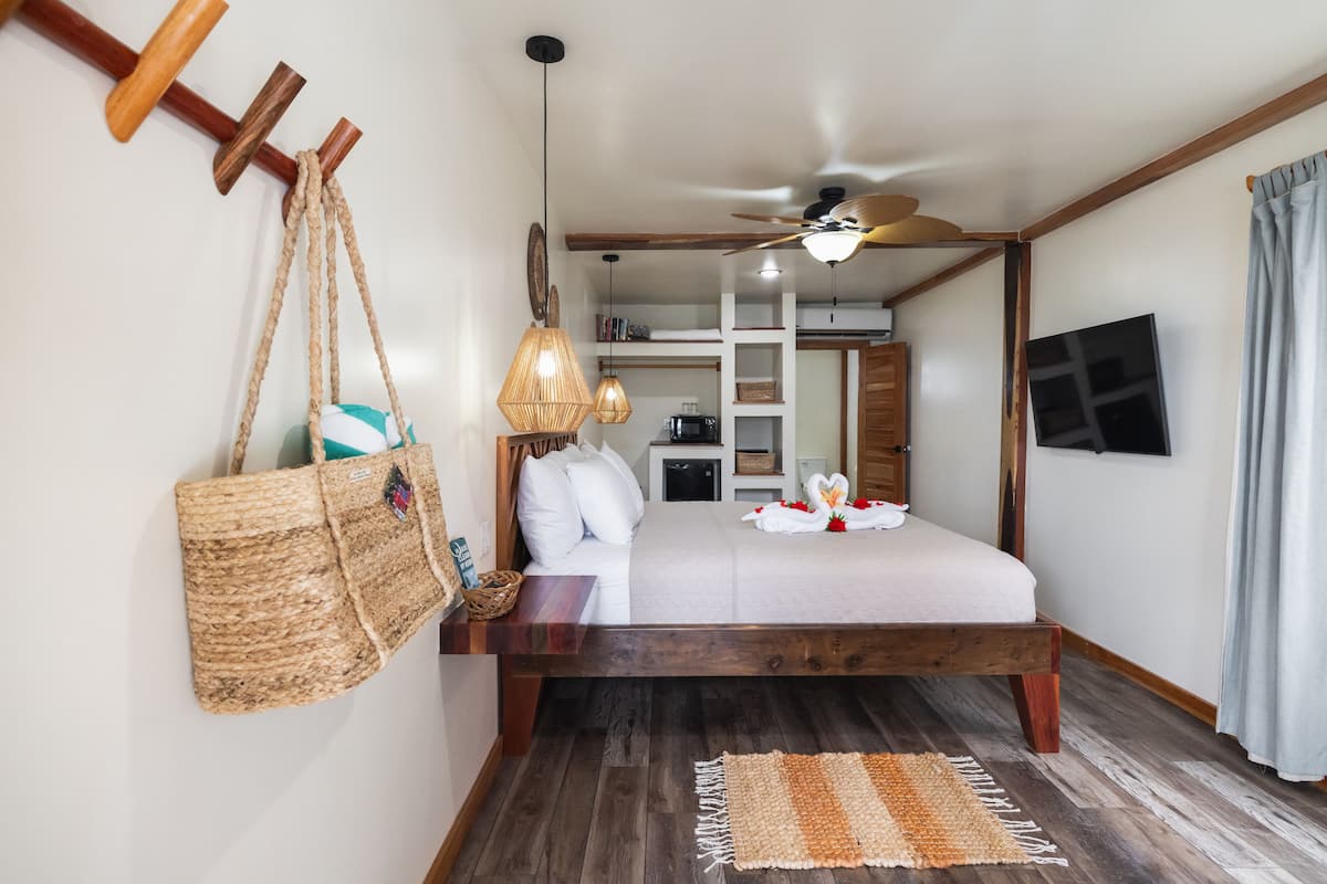 A bedroom with a wooden bed, a ceiling fan, a TV, and a woven bag hanging on the wall.