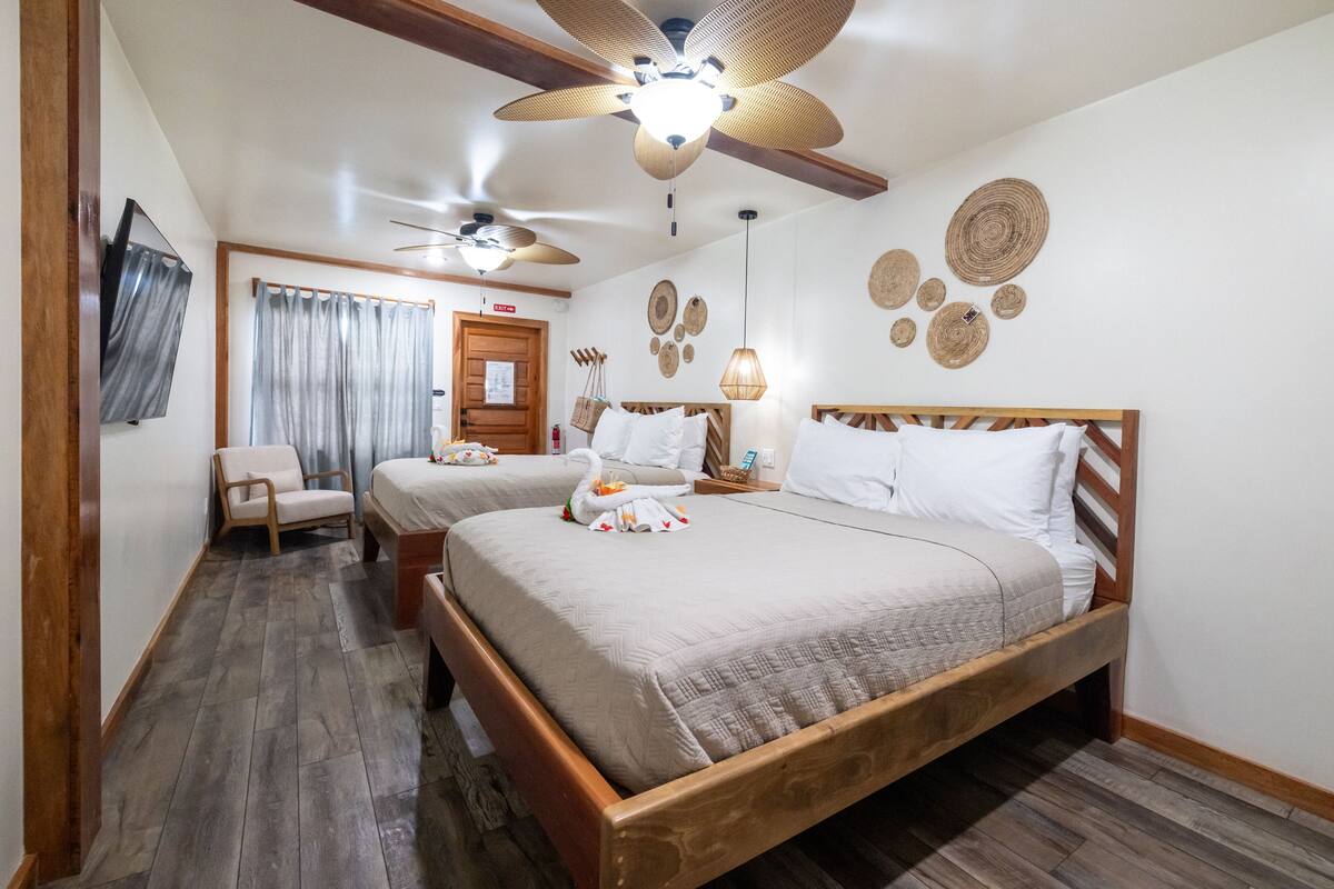 A bedroom with two beds, wooden flooring, ceiling fans, and wall decor.