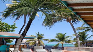 A poolside area with lounge chairs and palm trees, overlooking a beach. - Ocean Tide Beach Resort (San Pedro)