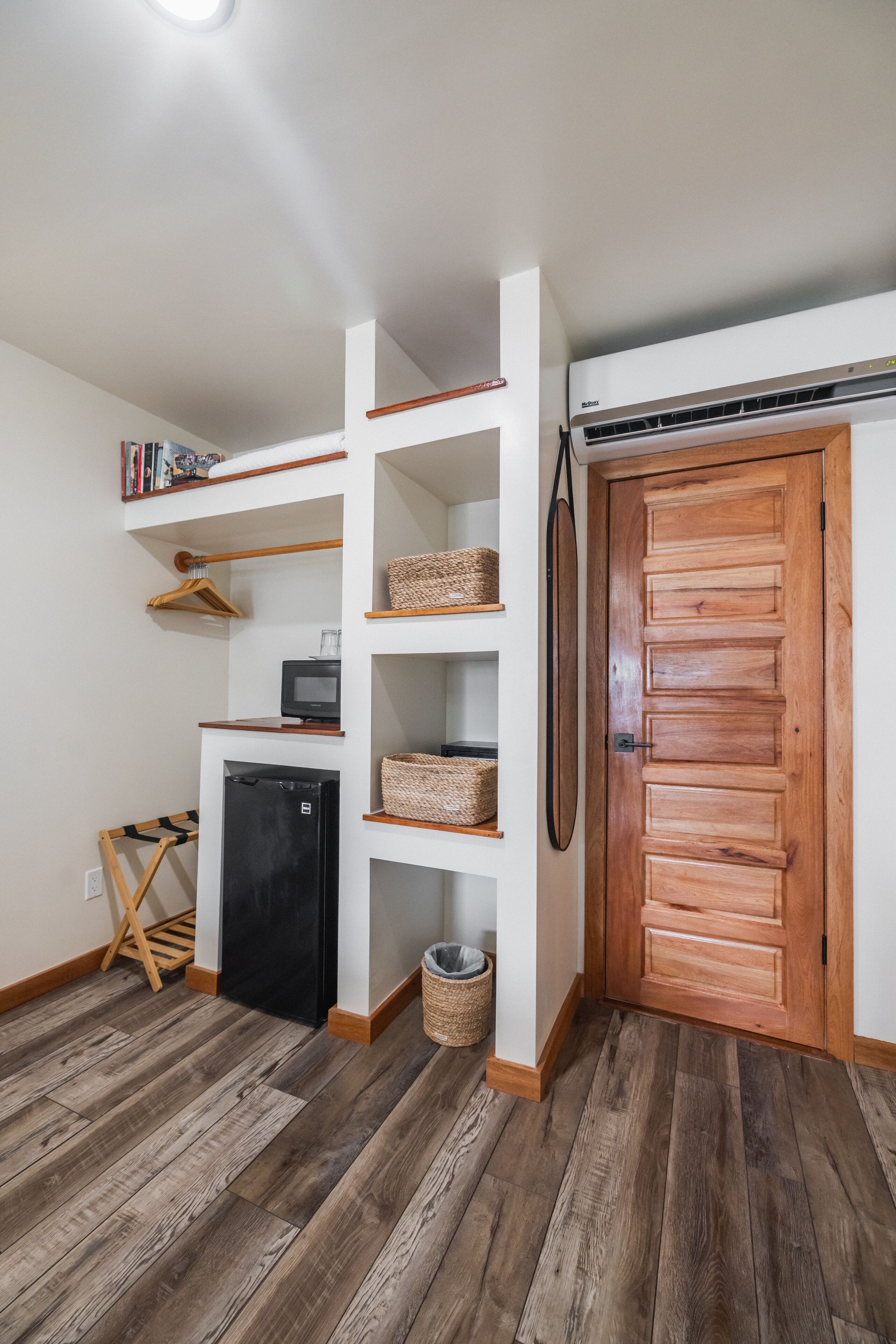 A compact room with a built-in shelving unit, a wooden door, and a small black refrigerator.