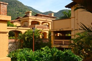A traditional building with arched balconies and a courtyard surrounded by lush greenery and mountains in the background. - Hotel Danza del Sol (Ajijic)