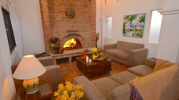 Una sala de estar con chimenea de ladrillo, dos sofás, una mesa de centro con fruta y una lámpara.