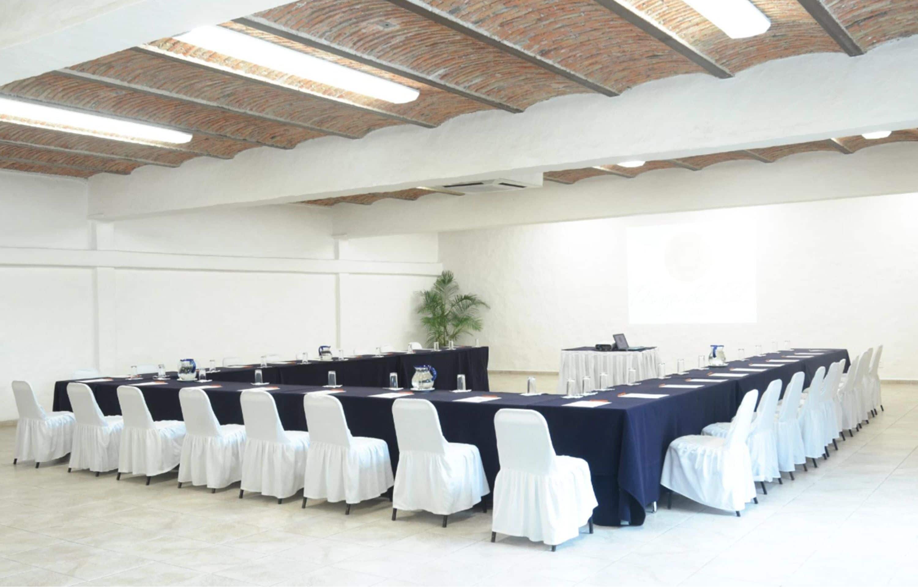 A conference room with a long table, white chairs, and a brick ceiling.