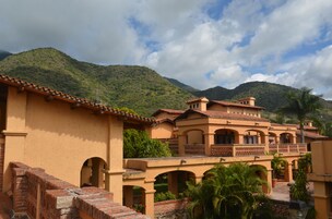 A traditional building with multiple arches and a courtyard, surrounded by lush greenery and mountains.