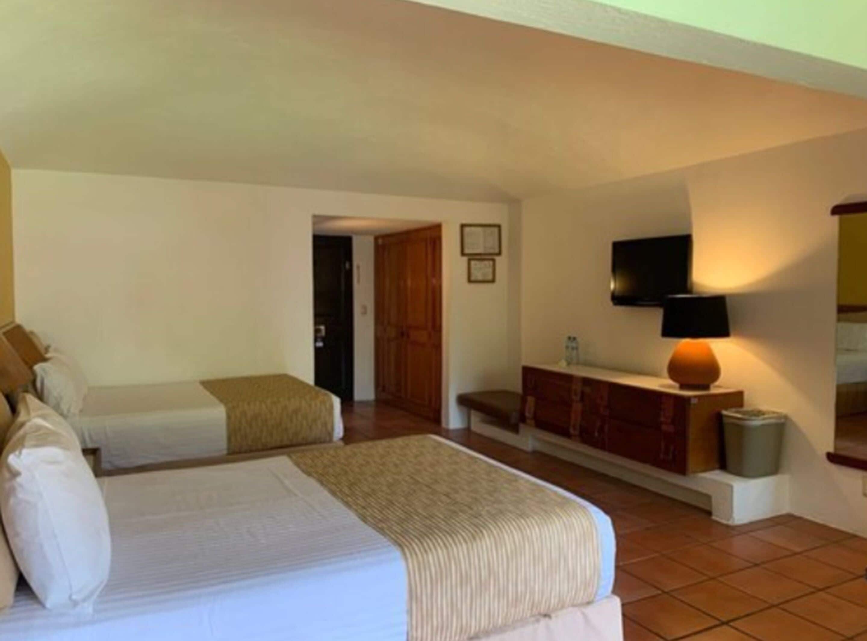A hotel room with two beds, a TV, a lamp, and a wardrobe.