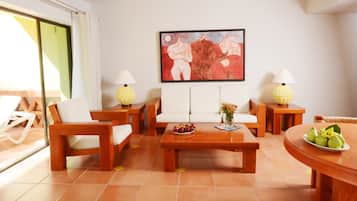 Una sala de estar con un conjunto de sofá, dos mesas auxiliares con lámparas, una mesa de centro con frutas y un cuadro en la pared.