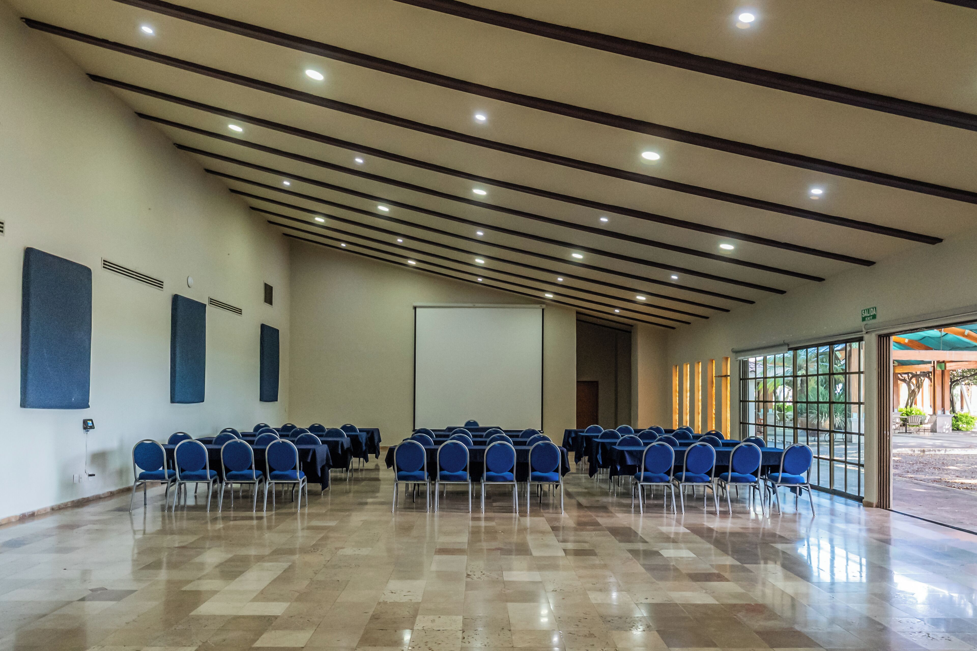 Una sala conferenze con file di sedie, uno schermo per proiezioni e un'ampia finestra.