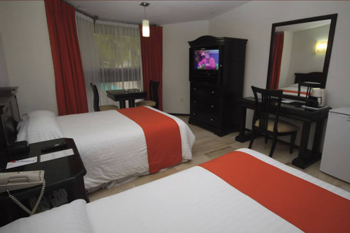Ett hotellrum med två sängar, ett skrivbord, en tv och ett kylskåp.