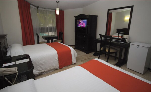 A hotel room with two beds, a desk, a television, and a refrigerator.