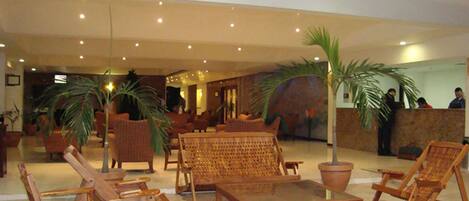 A lobby with wicker furniture, potted plants, and a reception desk.