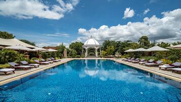 A pool with lounge chairs and umbrellas, a gazebo, and lush greenery.