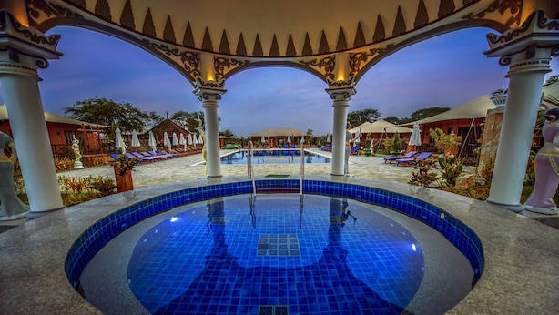 A circular pool with blue tiles, surrounded by white columns and arches, with lounge chairs and umbrellas in the background. - Bagan Lodge (Nyaung-U)