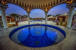 A circular pool with blue tiles, surrounded by white columns and arches, with lounge chairs and umbrellas in the background. - Bagan Lodge (Nyaung-U)