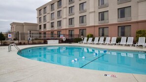 Una piscina con sillones de descanso, una valla y un edificio al fondo.