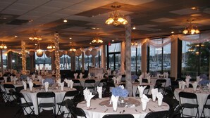 Un salón de banquetes con mesas redondas dispuestas para un evento formal, con manteles blancos, sillas negras y centros de mesa florales.