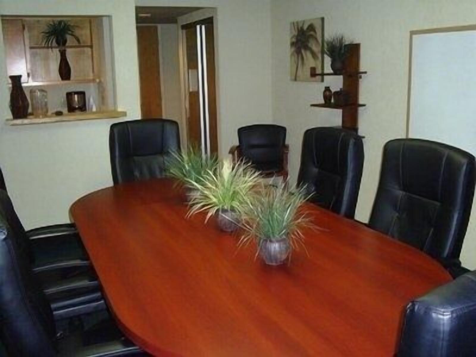 Un salón de conferencias con una mesa de madera, sillas de cuero negro y plantas en macetas.