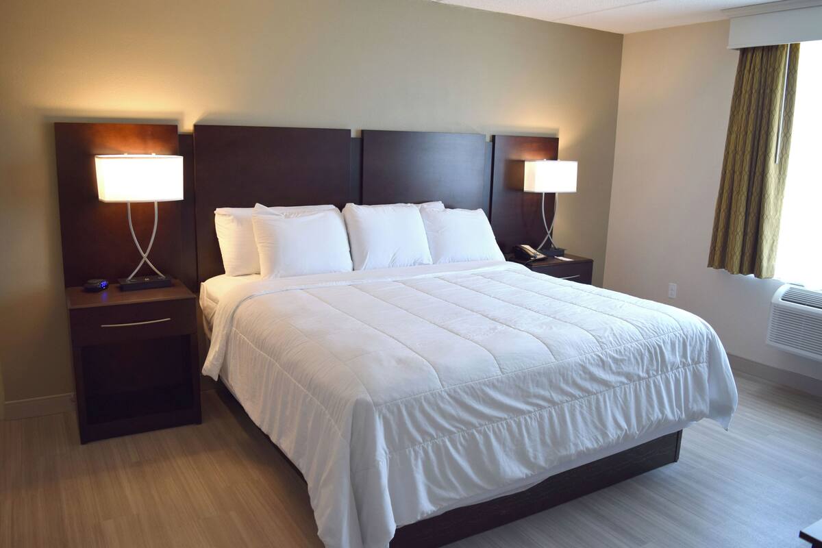 Quarto de hotel com uma cama grande, duas mesas de cabeceira e duas luminárias fixadas na parede.