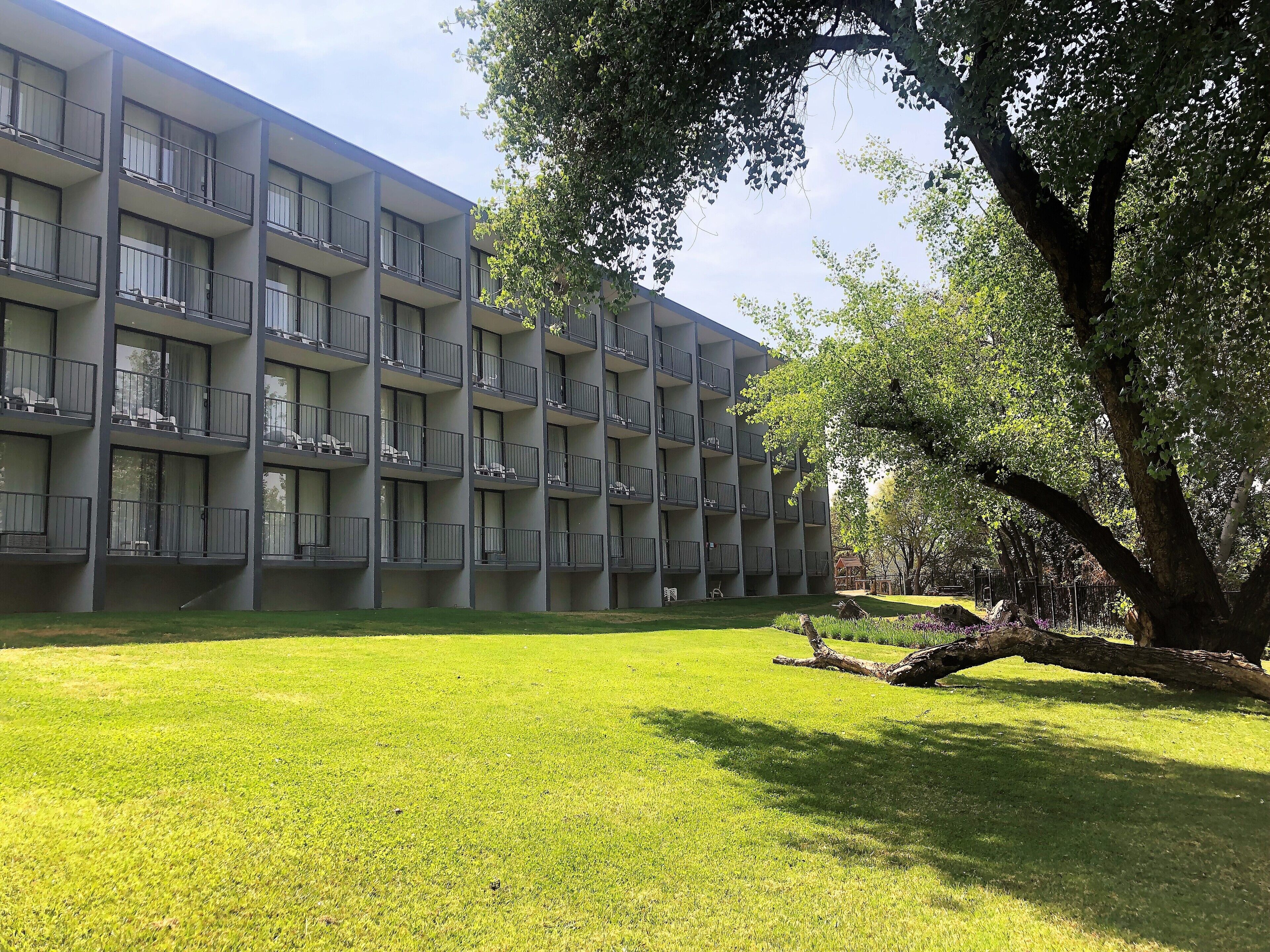 A multi-story building with balconies, a grassy courtyard, and trees.