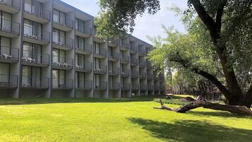 A multi-story building with balconies, a grassy courtyard, and trees.