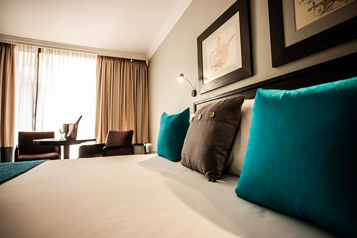 A hotel room with a large bed, two chairs, a small table, and a window with curtains.