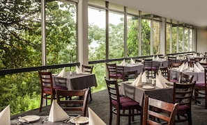 A restaurant with tables set for dining, large windows, and a view of trees. - Avani Maseru Hotel (Maseru)
