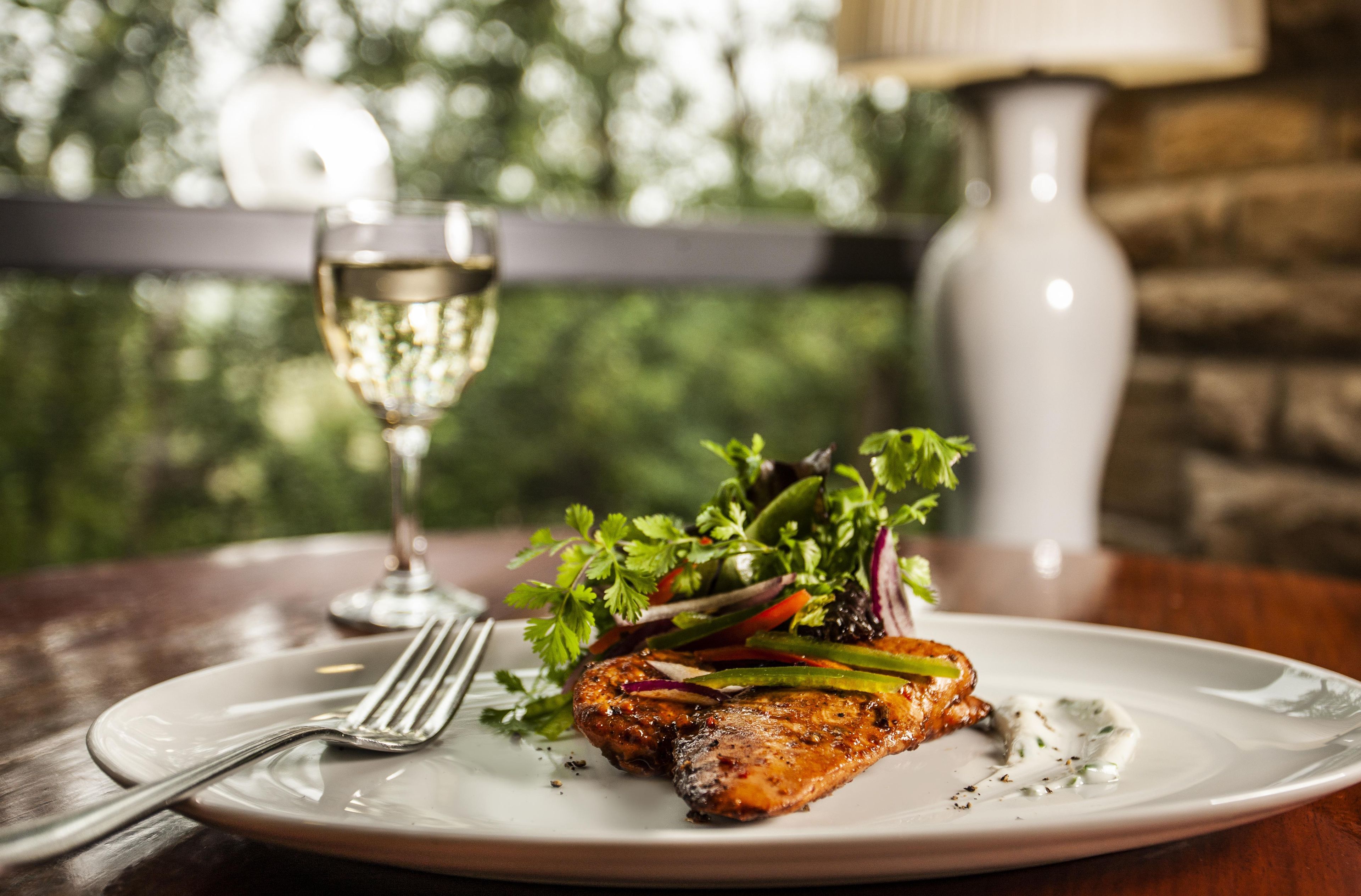 Une assiette contenant un poisson grillé, une salade et un verre de vin blanc, le tout posé sur une table en bois.
