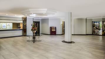 A spacious lobby with a reception desk, a decorative vase with flowers, a bookcase, and a shop display.