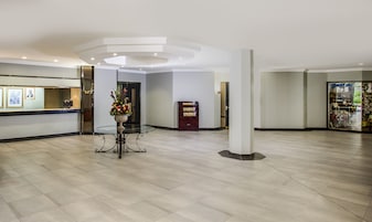 Un hall amplio con una mesa de recepción, un jarrón decorativo con flores, una estantería y un escaparate.