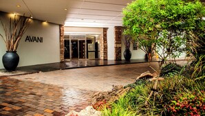 A hotel entrance with a brick pathway leading to a glass door, surrounded by greenery and potted plants. - Avani Maseru Hotel (Maseru)