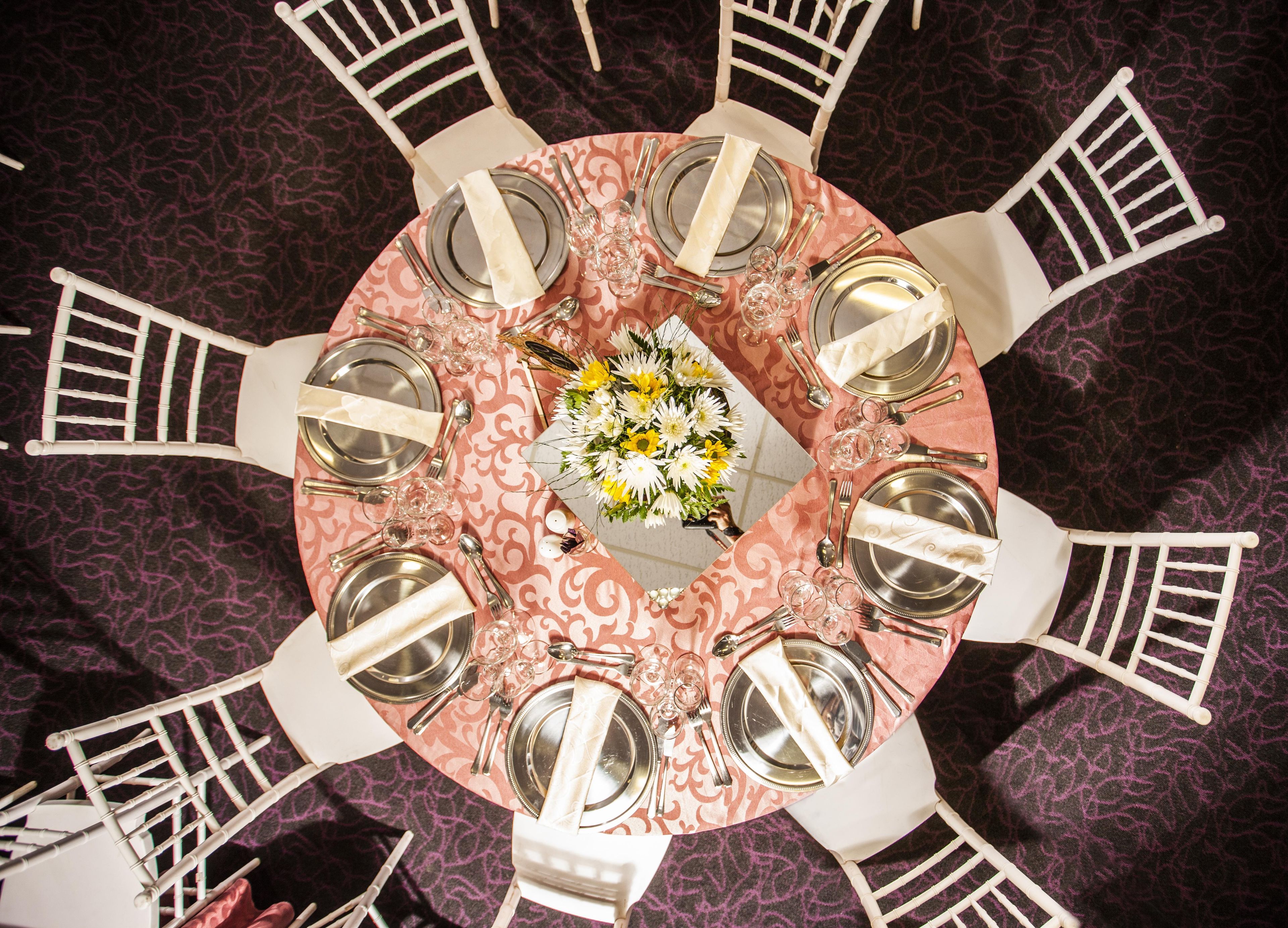Una mesa redonda con un centro de mesa floral, rodeada de sillas blancas.